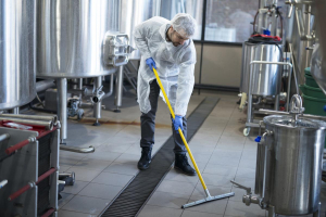 Professional cleaner wearing protection uniform cleaning floor of production plant.